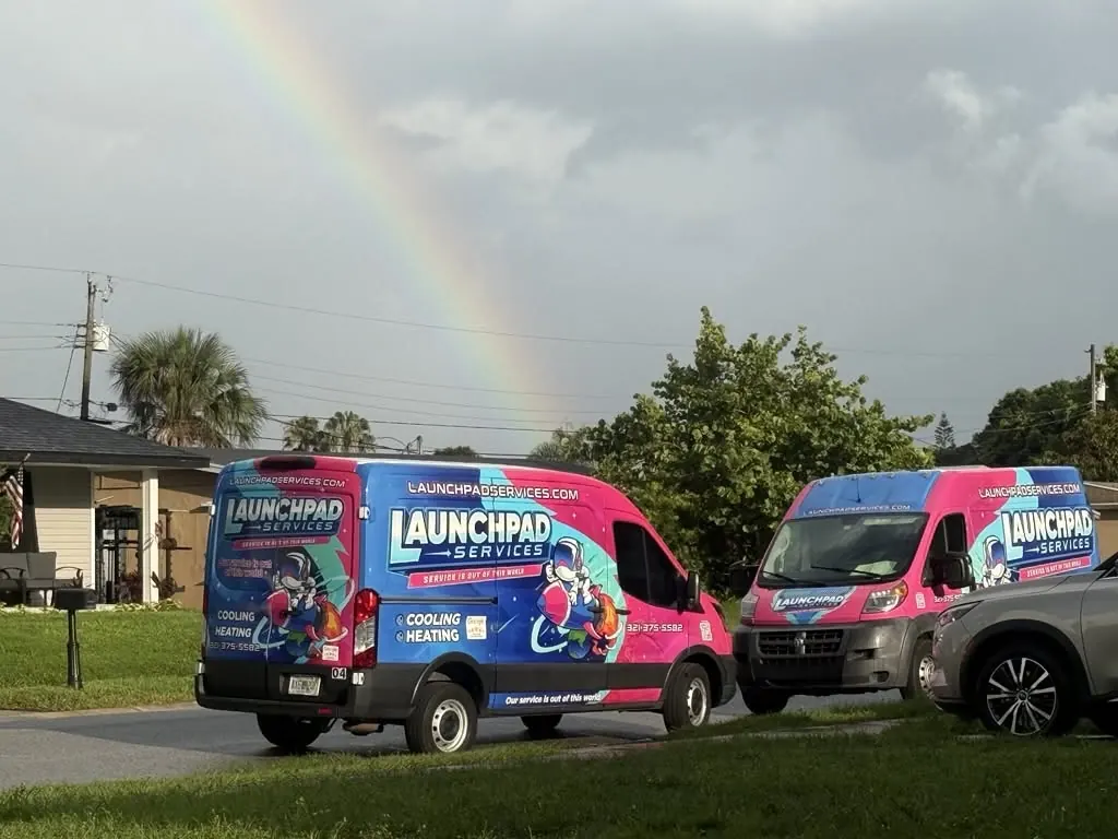 Two Launchpad Services vans parked under a rainbow in a Brevard County neighborhood